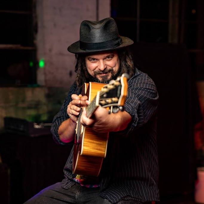 Musician,  Michael Doussan, wearing top hat, holding a guitar pointed at the camera